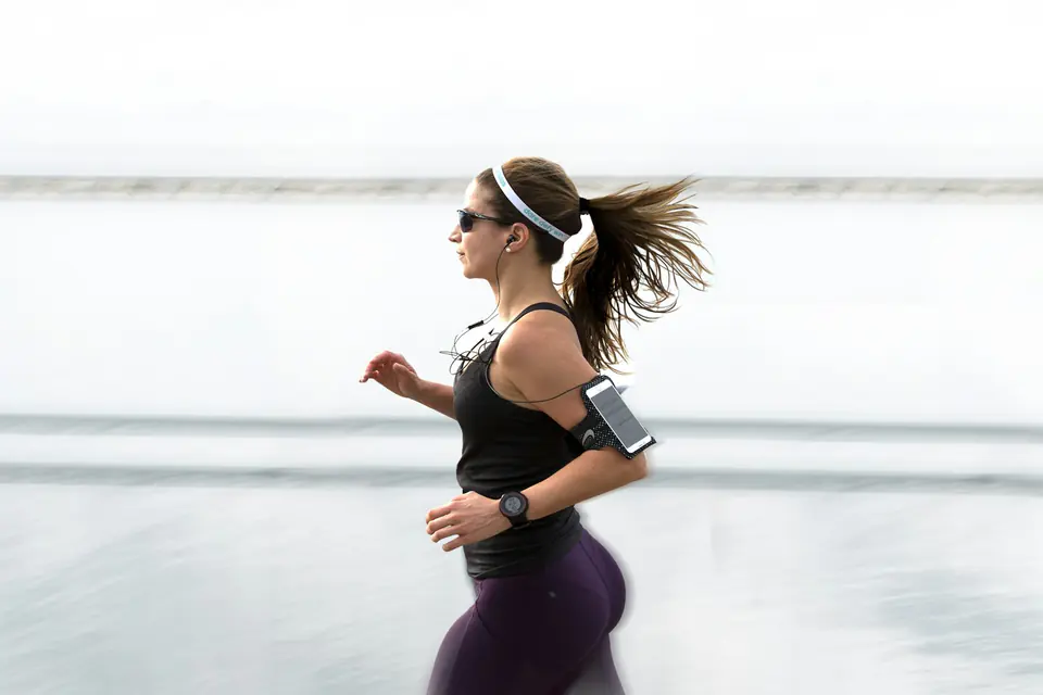 A runner in a black top and cap runs outdoors with a phone armband.