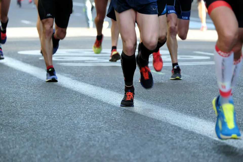 Runners' legs at a race start line on asphalt.