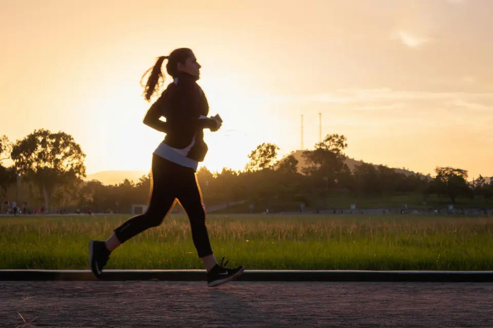 A runner silhouetted against a sunrise on a park path.