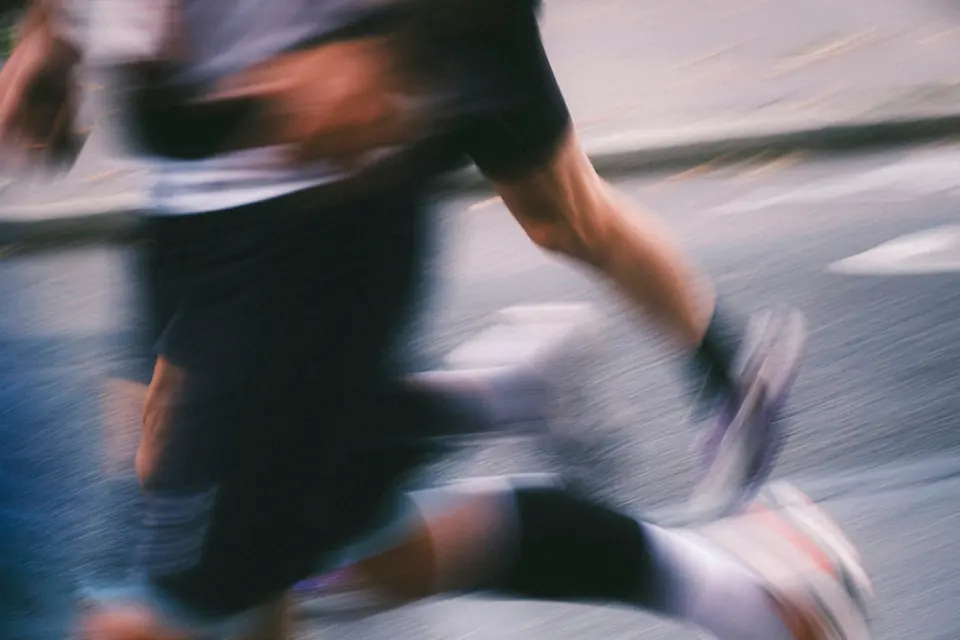 A runner's legs and shoes mid-stride, motion-blurred on a dark road.