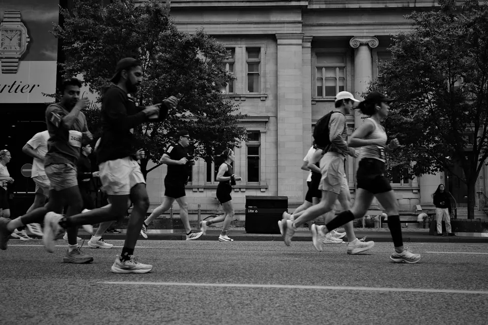 A group of runners crossing a city street beside stone buildings.