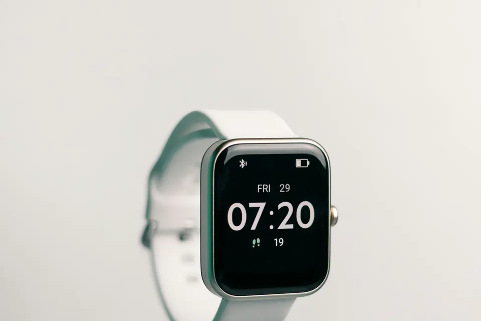 A smartwatch with a black face showing the time, resting on a pale surface.